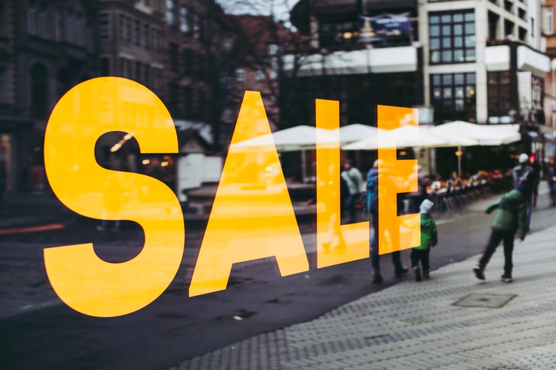 Reflection of people in the window of a store promoting sales.